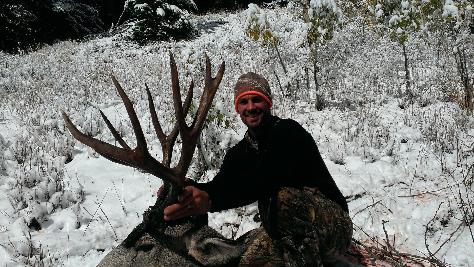 A man is kneeling down in the snow holding a large deer