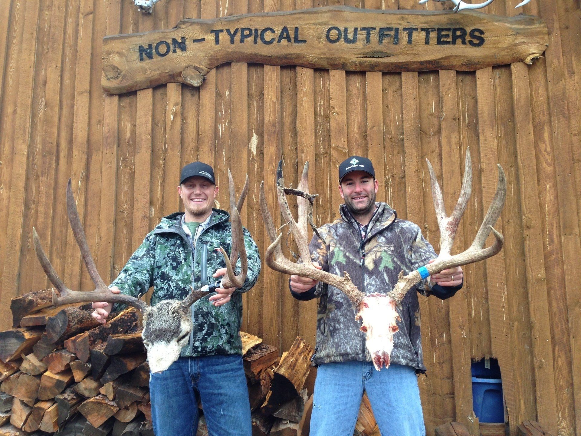 Two men holding deer antlers in front of a sign that says non-typical outfitters