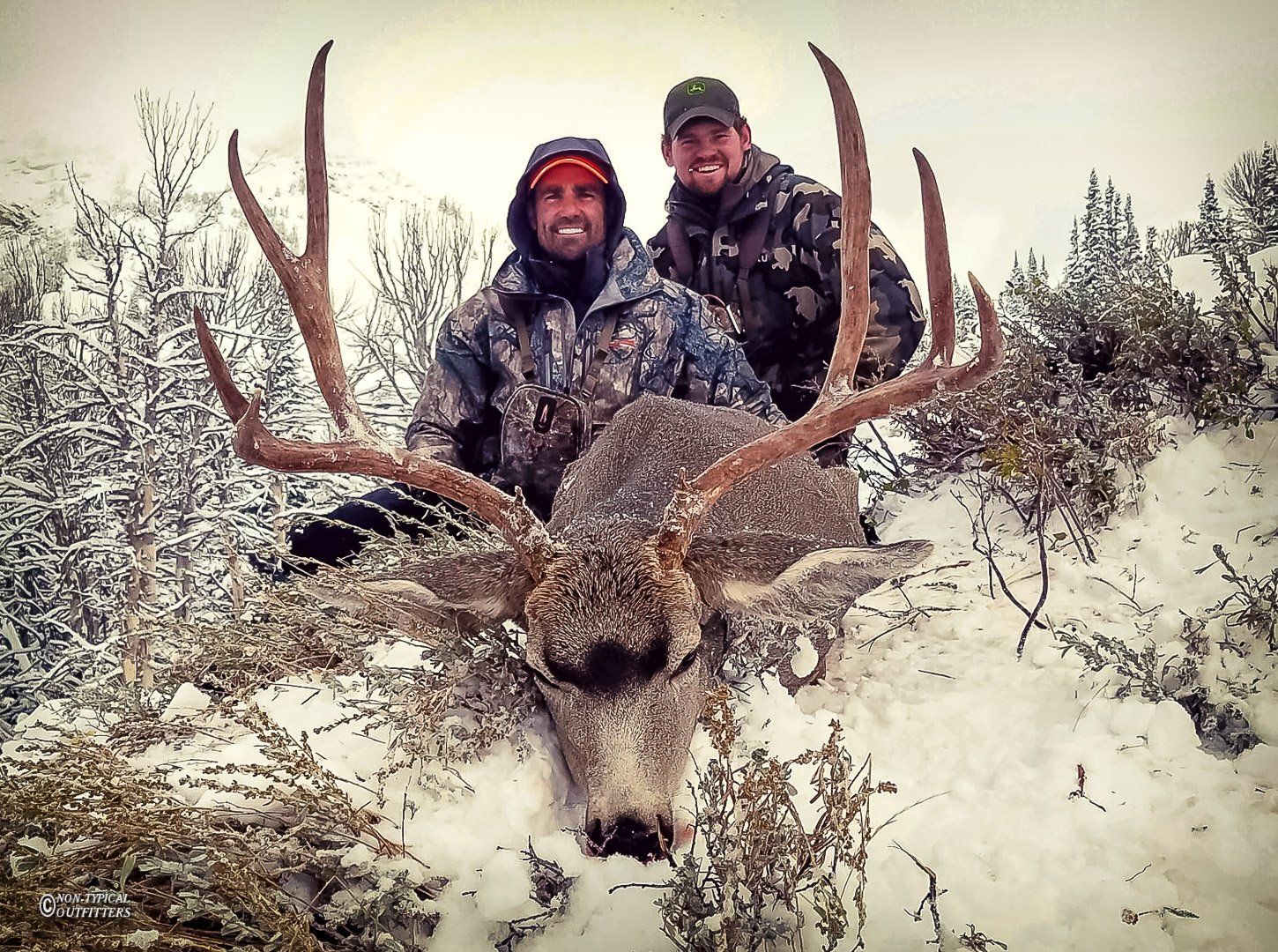 Two men pose with a large deer in the snow