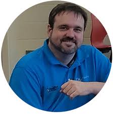 A man with a beard is wearing a blue shirt and smiling.