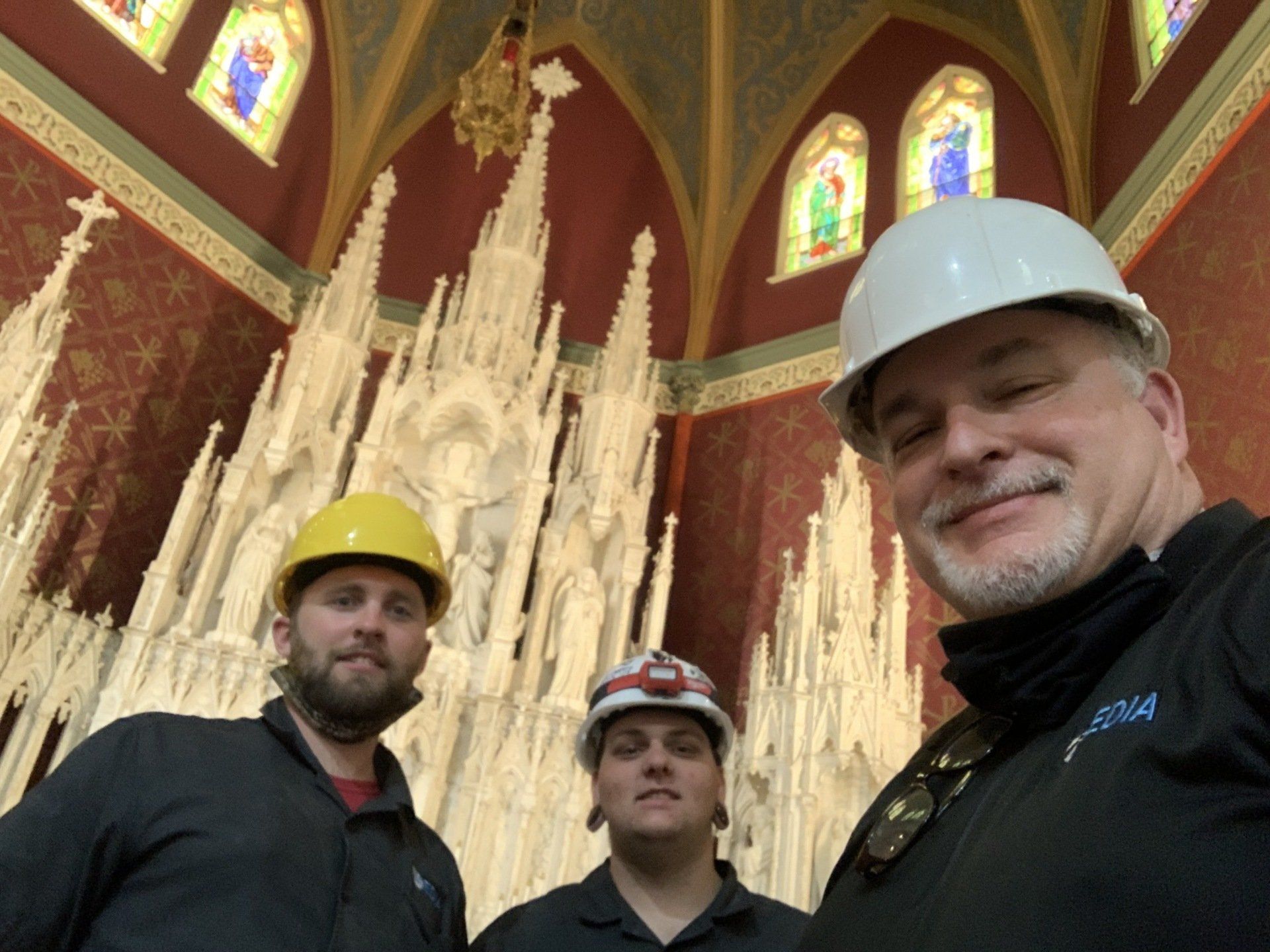 Three men wearing hard hats are posing for a picture in a church