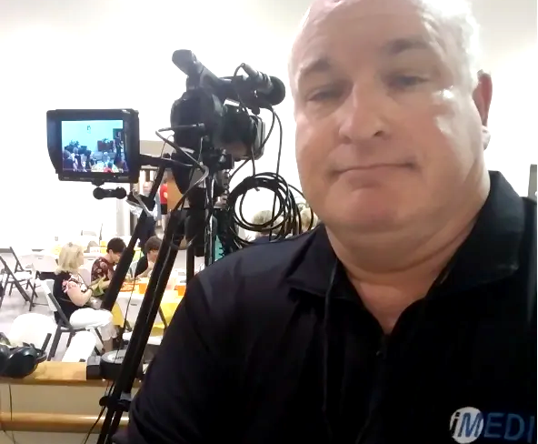 A man in a black shirt is standing in front of a video camera