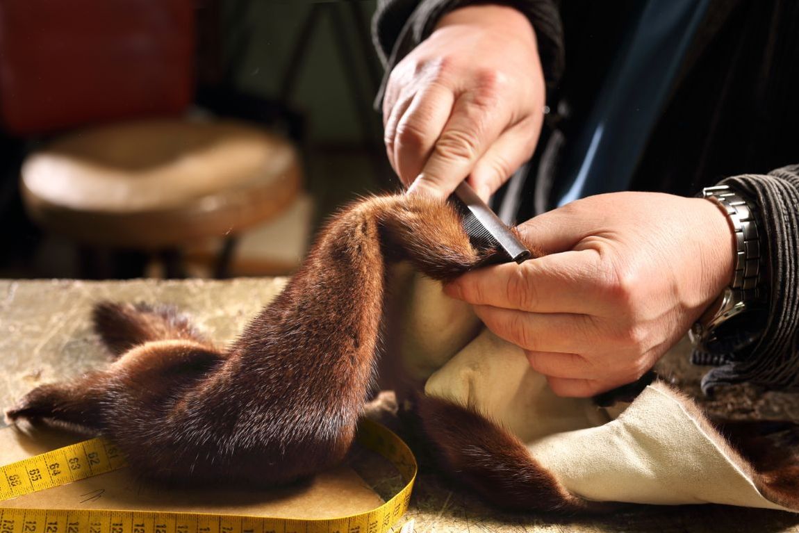 Mani che cuciono un tessuto di pelliccia marrone con ago e filo su un tavolo da lavoro.