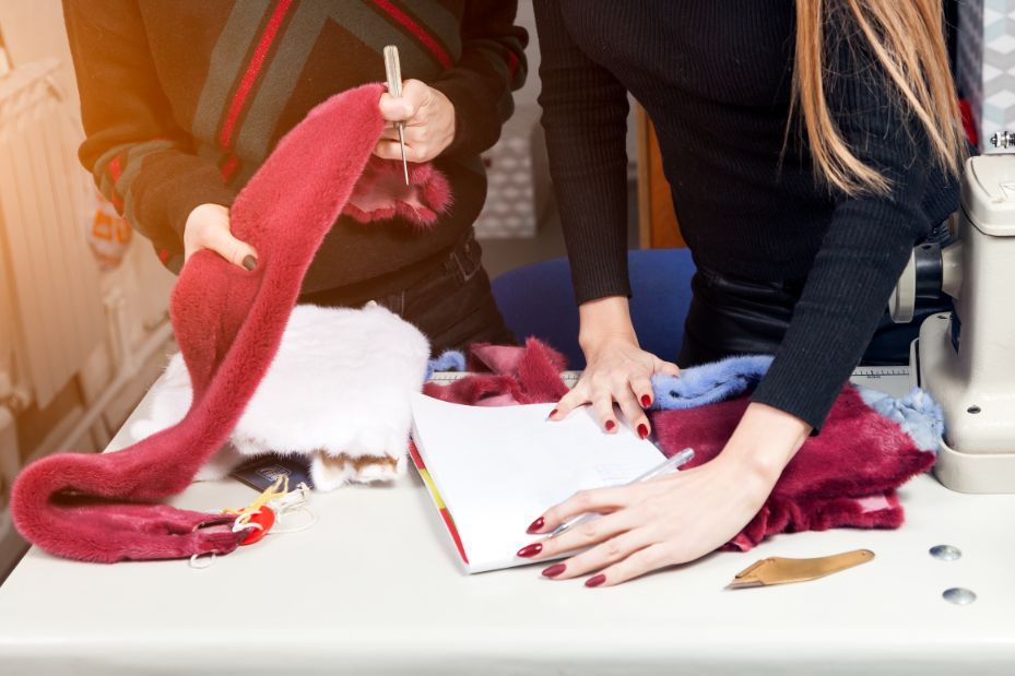 Persone che assemblano un cappello di Babbo Natale rosso e bianco su un tavolo con forbici e materiali per il bricolage.