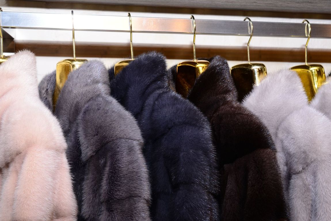 Pellicce bianche, grigie, blu e nere appese in fila su grucce dorate.