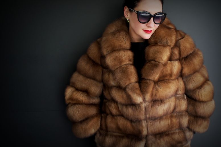 Donna con occhiali da sole e cappotto di pelliccia marrone su sfondo scuro
