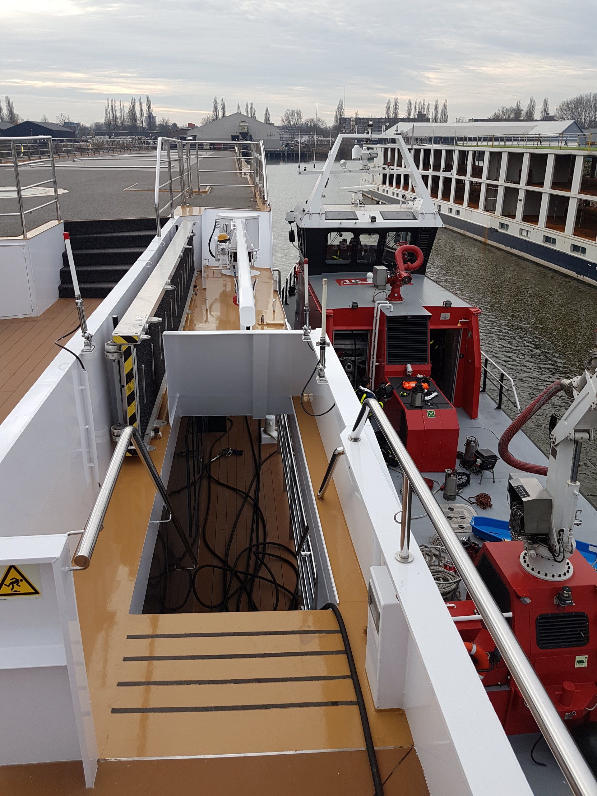Uitzicht op het scheepsdek met trappen en apparatuur, aangemeerd nabij de industriële waterkant.