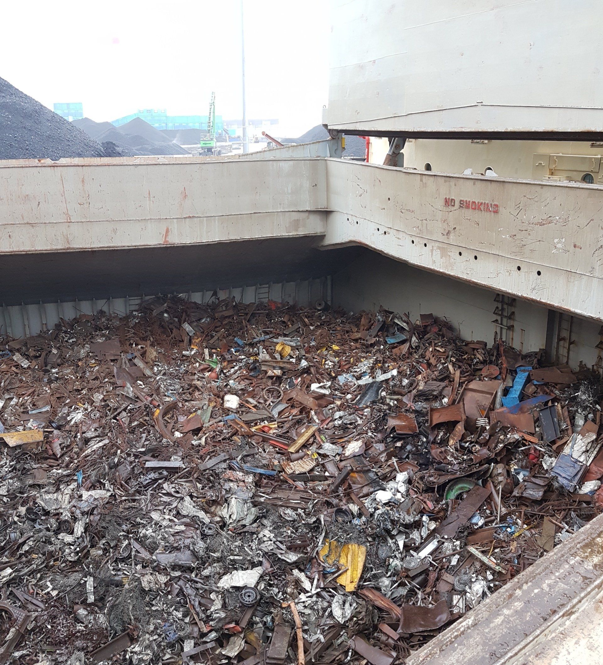 Schrootmetaal vult een grote industriële container, onder een betonnen constructie.