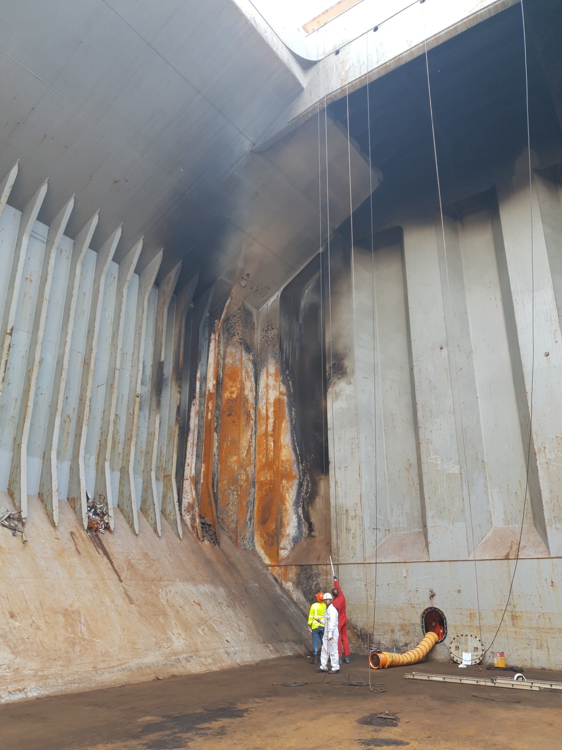 Interieur van het vrachtruim van een schip, verkleuring door een brand, met twee personen in beschermende pakken.