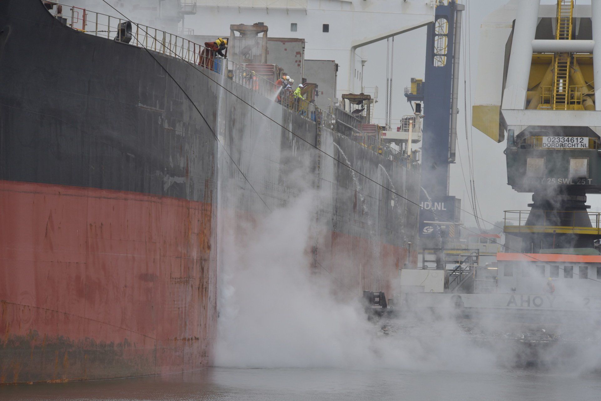 Een vrachtschip wordt gekoeld. Er spuit water langs de zijkant, waardoor een mistwolk ontstaat.