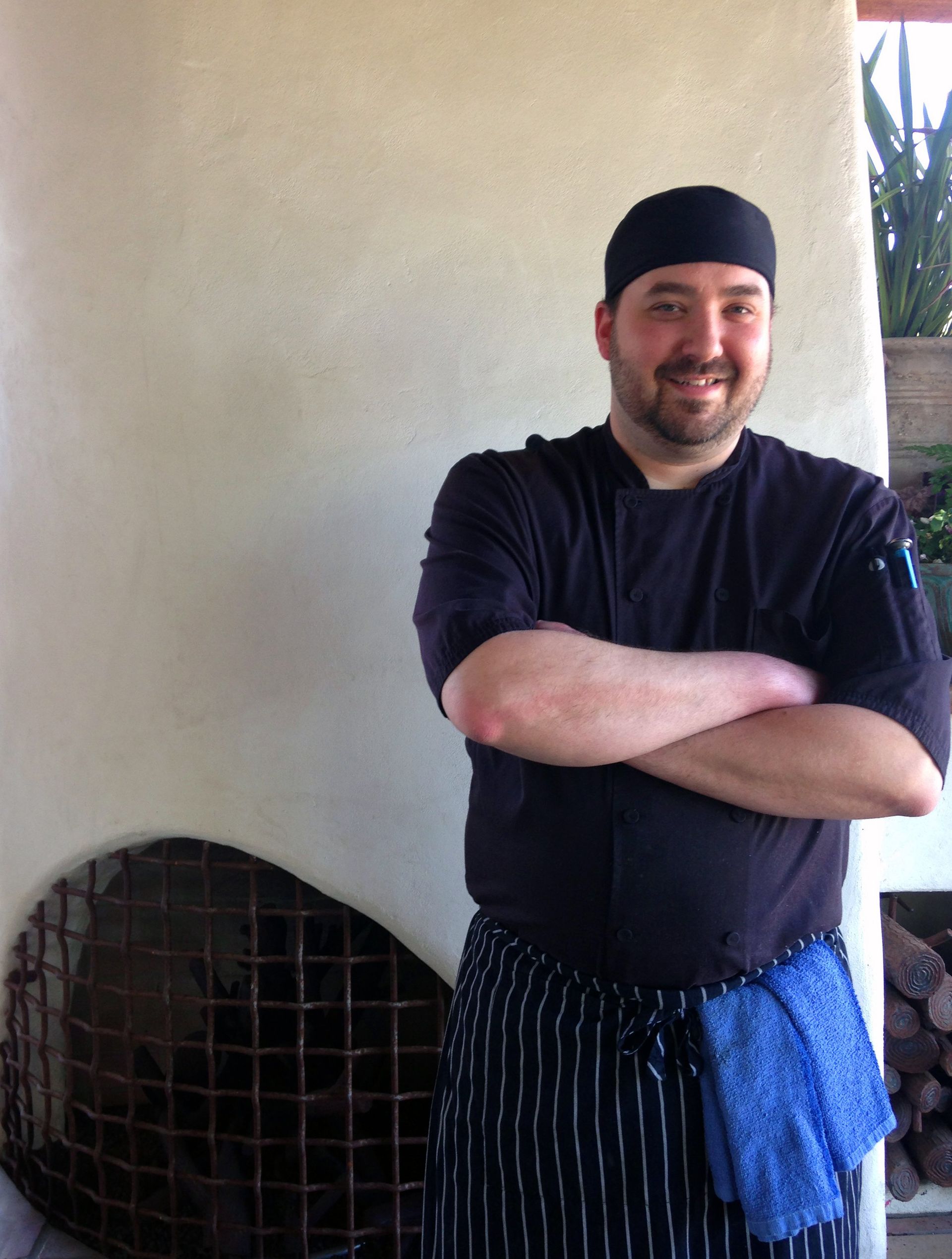 A man in a chef 's uniform is standing with his arms crossed