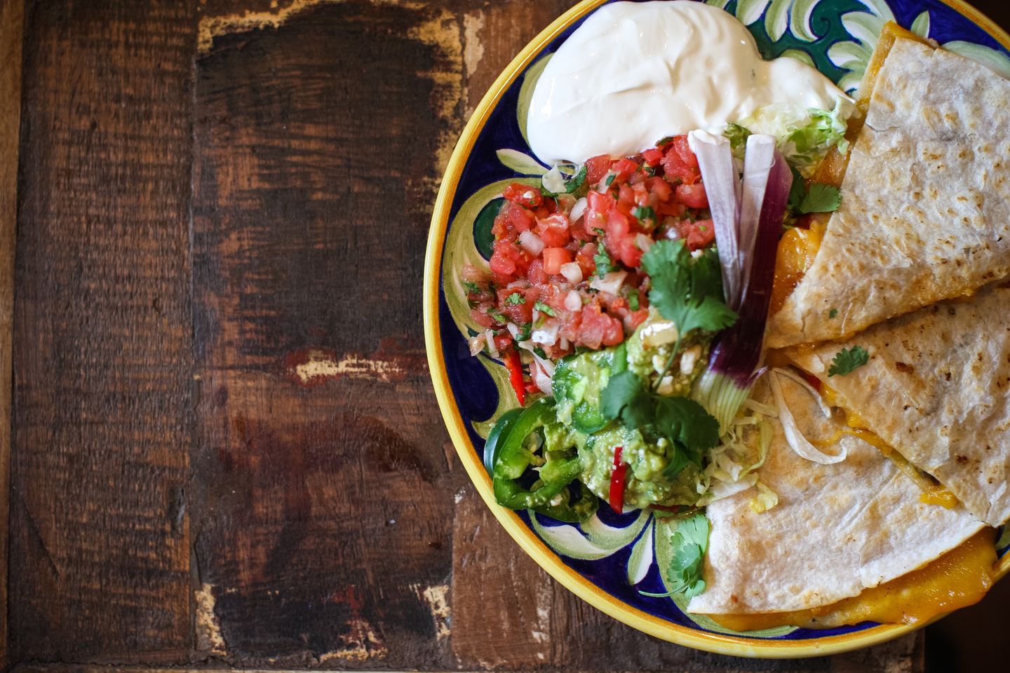 A plate of quesadillas with guacamole and sour cream on a wooden table.