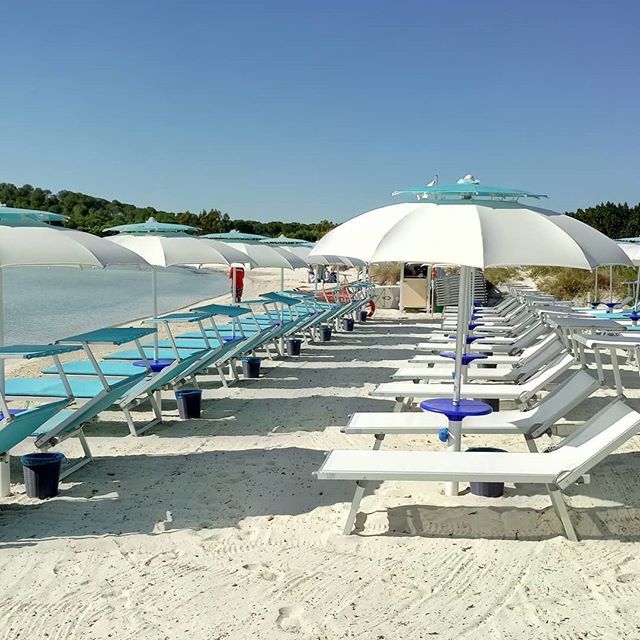 spiaggia con lettini bianchi e azzurri e ombrelloni aperti