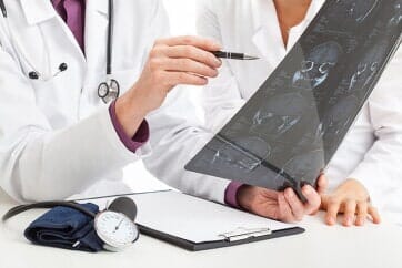 Doctors examining X-ray, pointing at results. Desk with clipboard, blood pressure cuff.