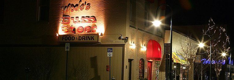 Nighttime storefront with a lit neon sign and brick building along a city street