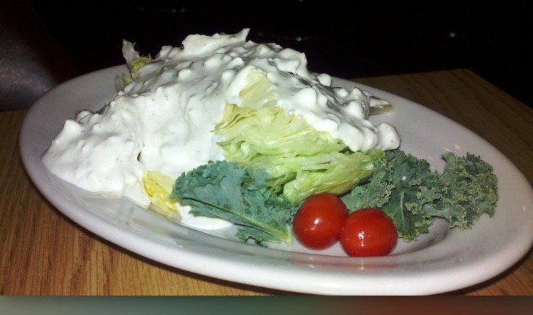 Plate of salad with lettuce, broccoli, cherry tomatoes, and a creamy white topping on a wooden table