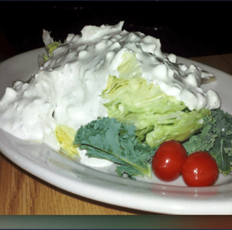White frosted cake slice on a plate, topped with whipped cream and garnished with cherries and mint leaves