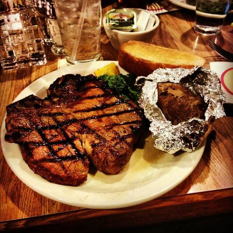 Grilled steak and baked potato with butter on a plate at a restaurant table