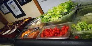 Salad bar with trays of vegetables, including cherry tomatoes, lettuce, and cucumbers, on a counter