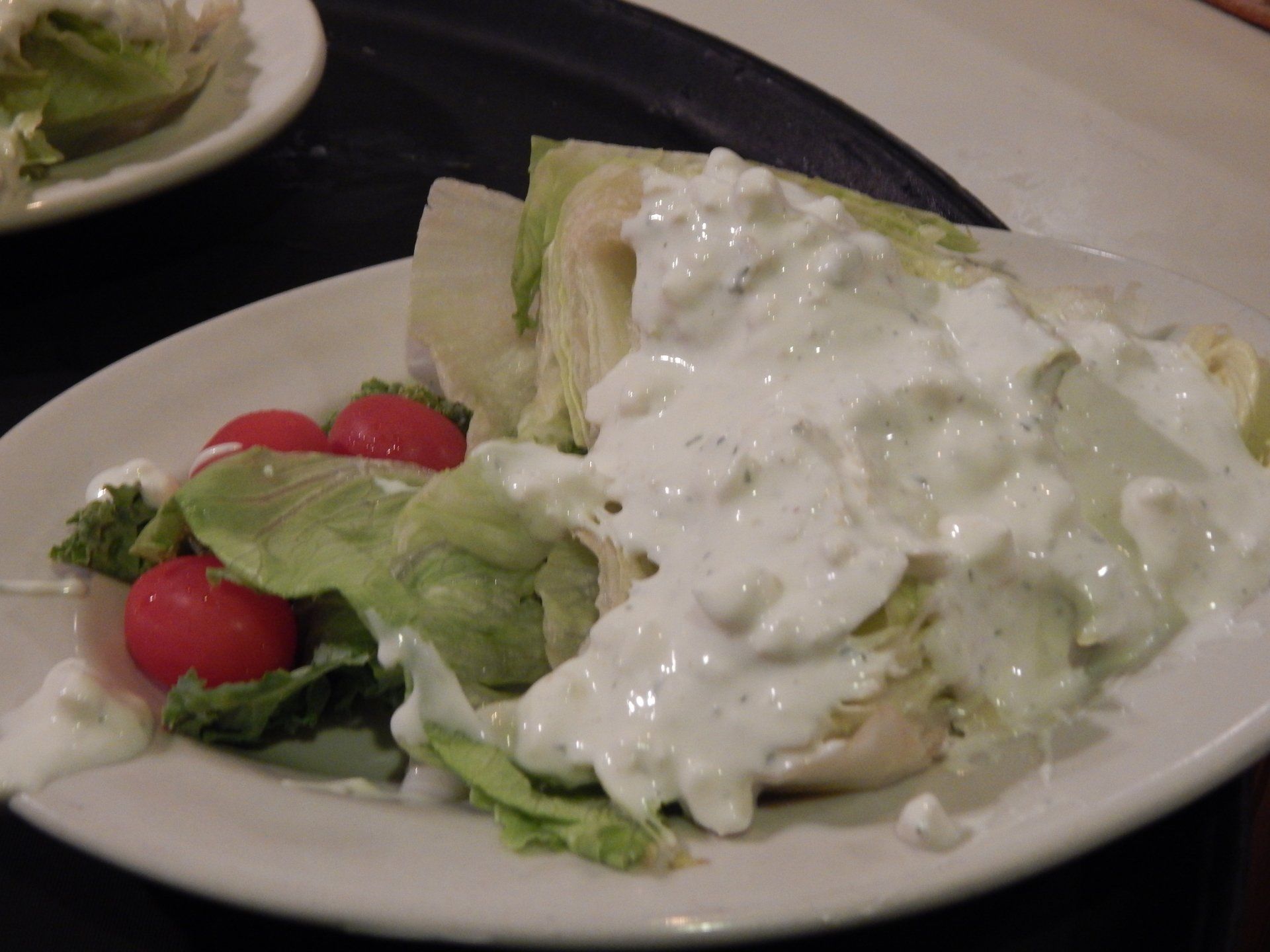 Plate of salad with lettuce, cherry tomatoes, and creamy dressing on a table