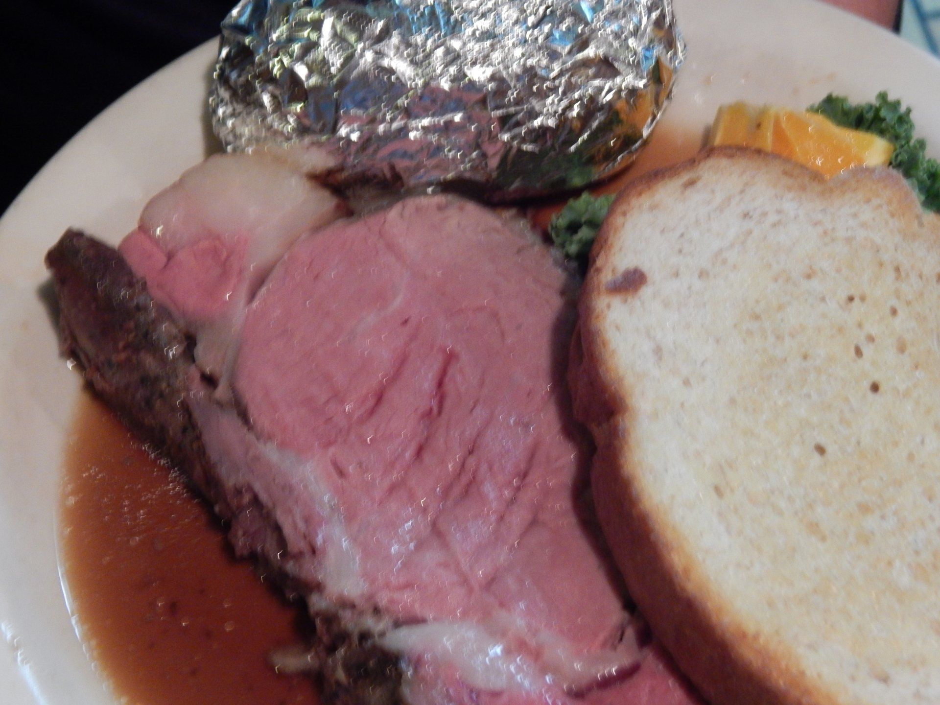 Plated roast beef with baked potato wrapped in foil and a slice of bread