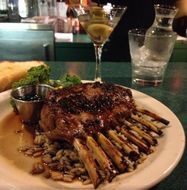 Grilled ribs on a plate with broccoli, sauce cup, and a martini glass on a restaurant table