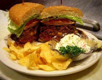 Oversized burger with chips and coleslaw on a white plate, with a metal cup in the background