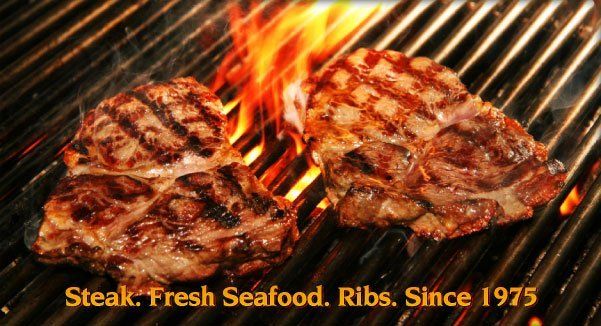Two grilled steaks on a barbecue grill with flames, text: “Steak, Fresh Seafood, Ribs Since 1975”