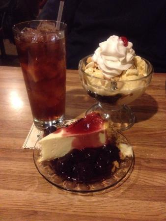 Dessert plate with cheesecake, ice cream sundae, and a tall glass of iced cola on a wooden table