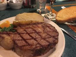 Grilled steak on a white plate with a baked potato, on a restaurant table with a wine glass and bread