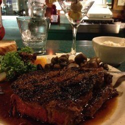 Grilled steak on a plate with mushrooms, parsley, a wine glass, and water glass on a restaurant table
