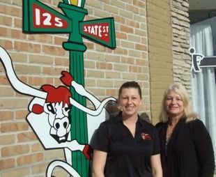 Two women standing by a school mascot mural beside a brick building sign