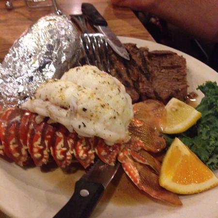 Platter of surf and turf with lobster, steak, rice, lemon wedges, and broccoli on a white plate