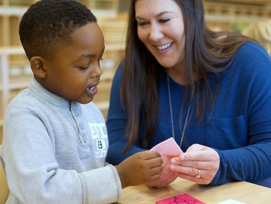 A montessori guide is showing a young boy a piece of paper.