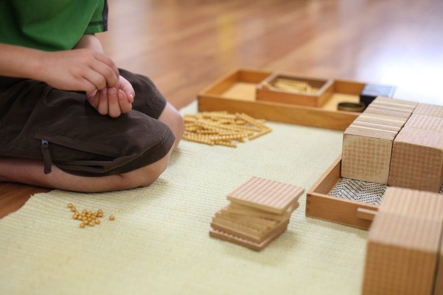 Child using wooden Montessori math materials on a rug.