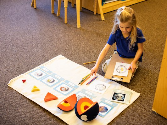 A little girl is sitting on the floor studing with a montessori model of the earth.