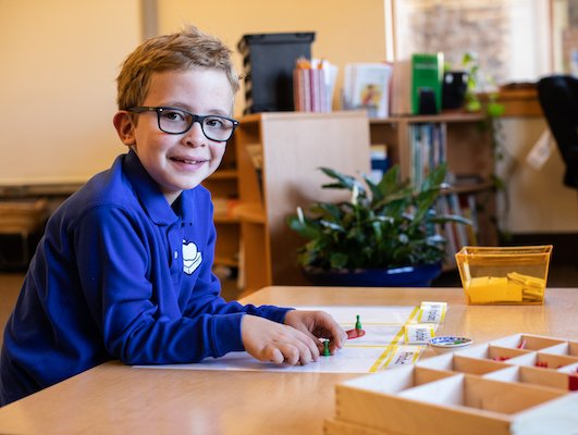 A young boy wearing glasses is sitting at a table in a classroom.