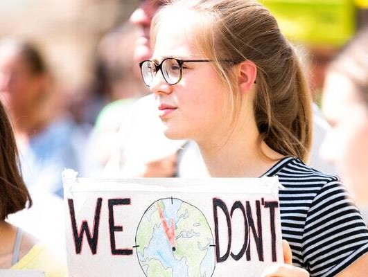 A young woman wearing glasses is holding a sign that says