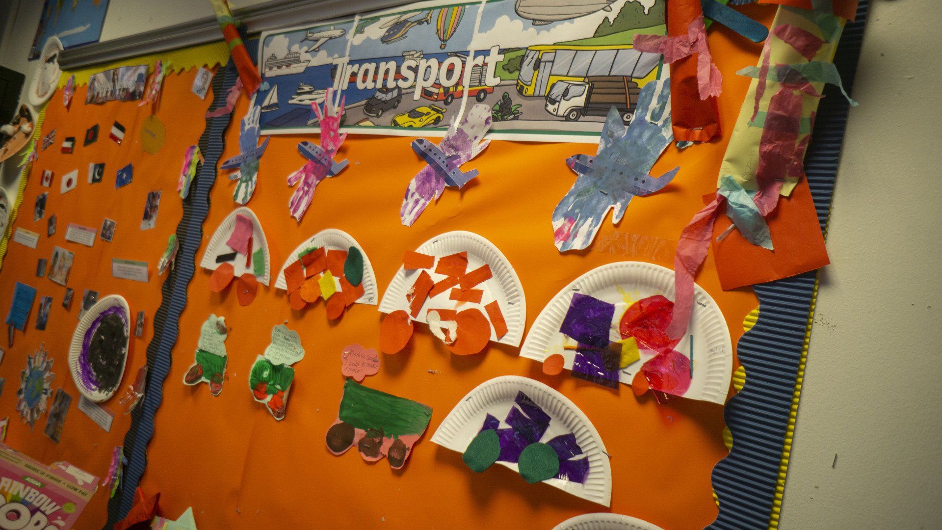 Colorful classroom art display about transport: planes, trains, and paper plate crafts on an orange background.
