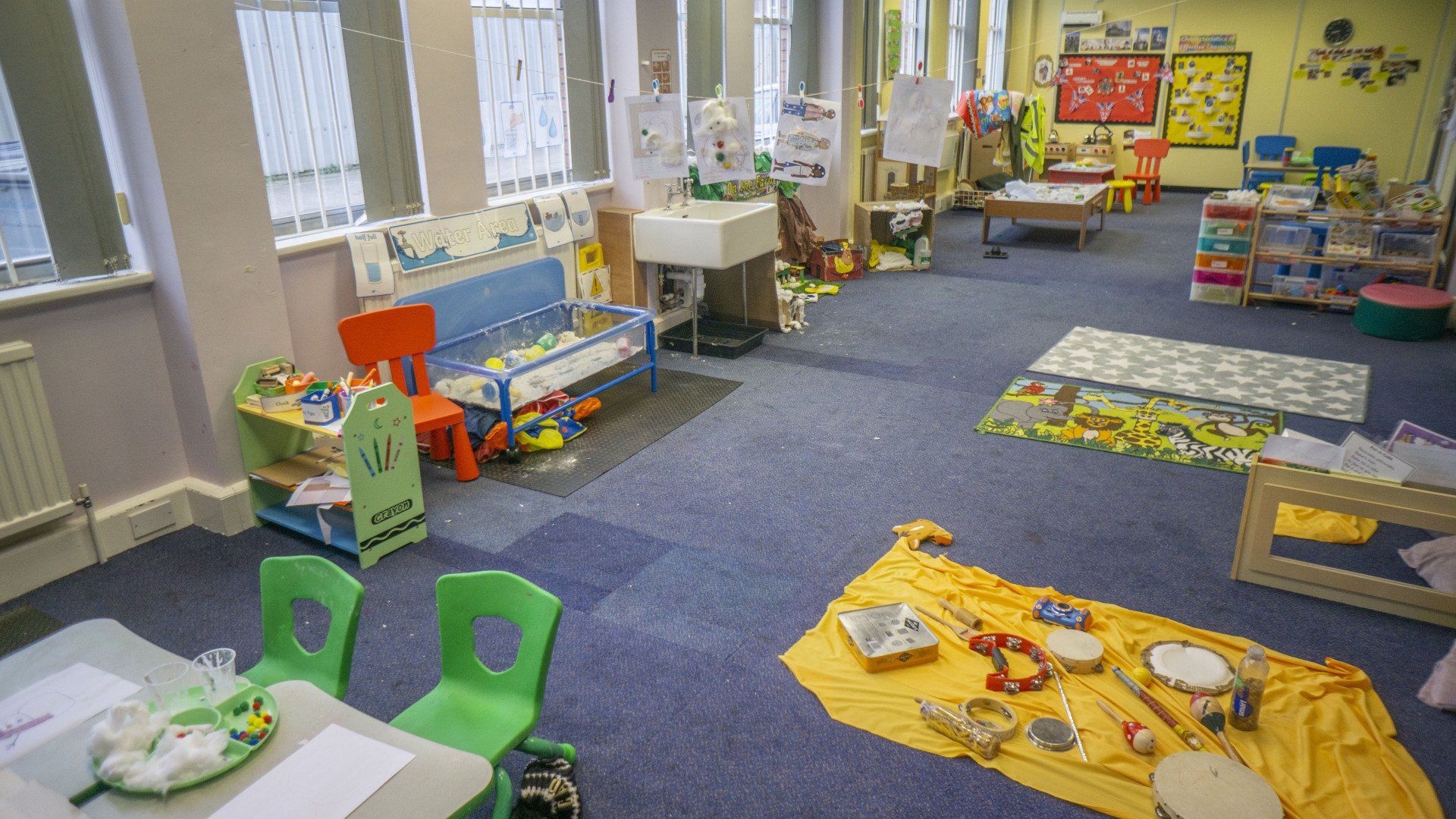 A brightly lit preschool classroom with toys, a seating area, and craft supplies on a blue carpet.