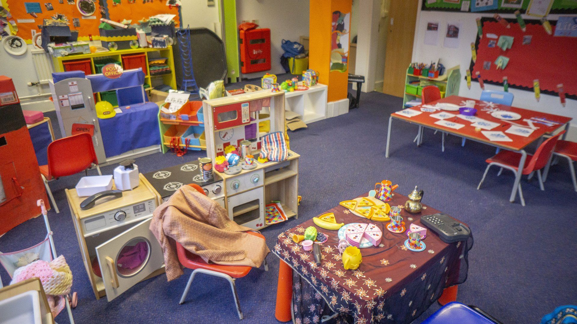 Interior of a brightly colored preschool classroom, toys, tables, chairs, and colorful decorations.