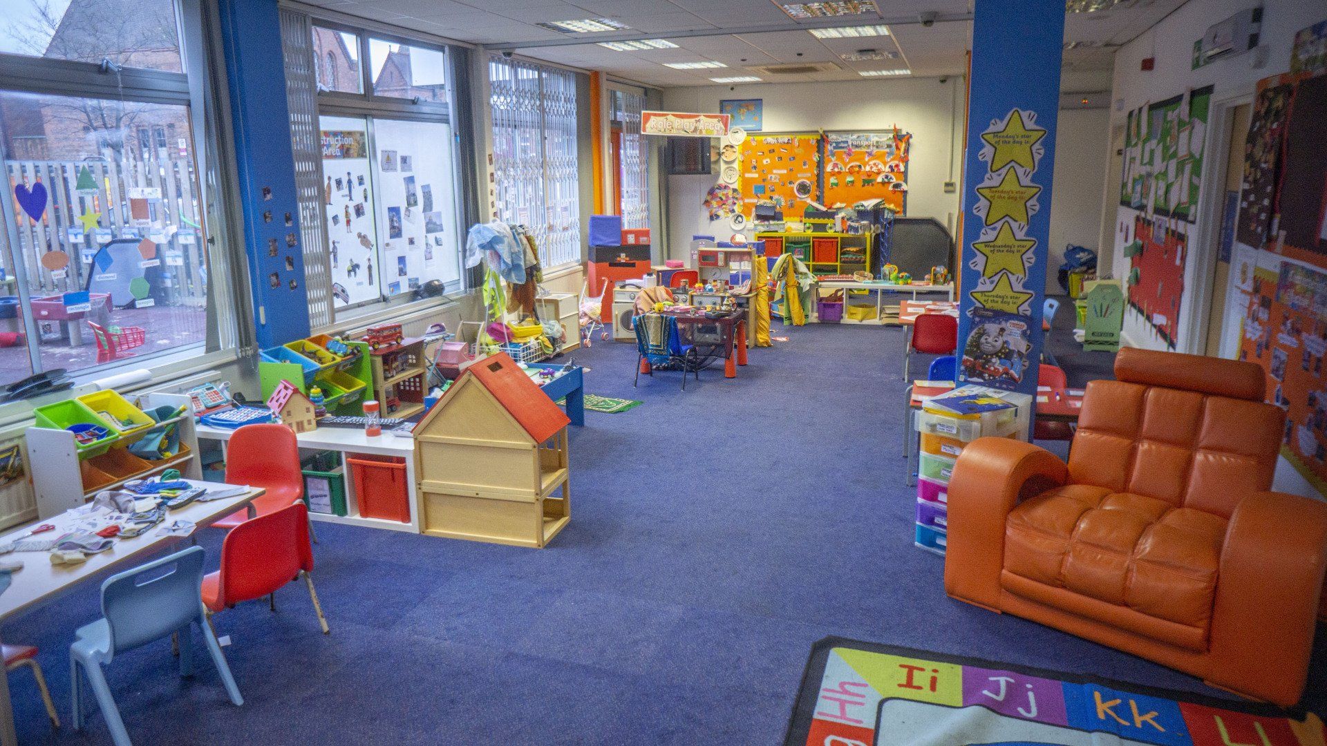 Interior of a colorful playroom. Toys, furniture, and art are scattered around the blue carpeted space.