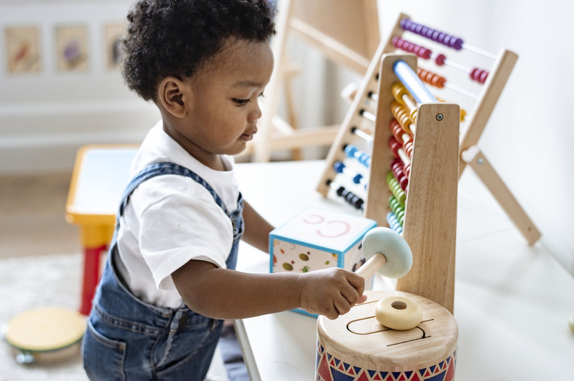 Child playing with wooden toys, including a drum, block, and abacus.