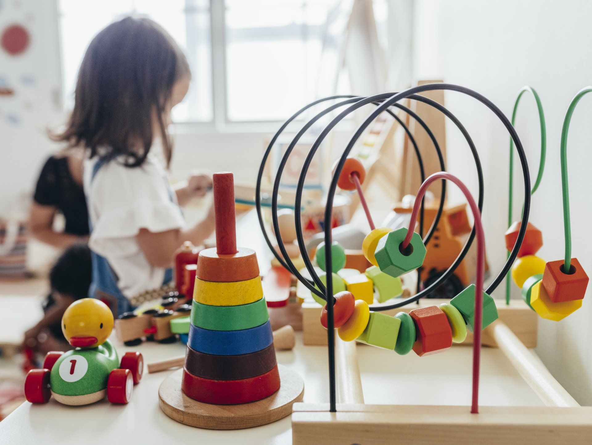 Child playing with colorful wooden toys on a table in a playroom.
