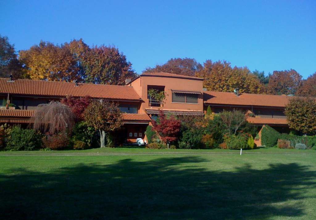 una grande casa con il tetto di tegole rosse si trova nel mezzo di un campo verde lussureggiante