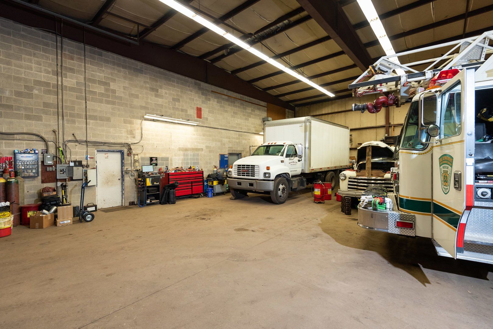 Interior of a garage with a fire truck, a box truck, and tools.