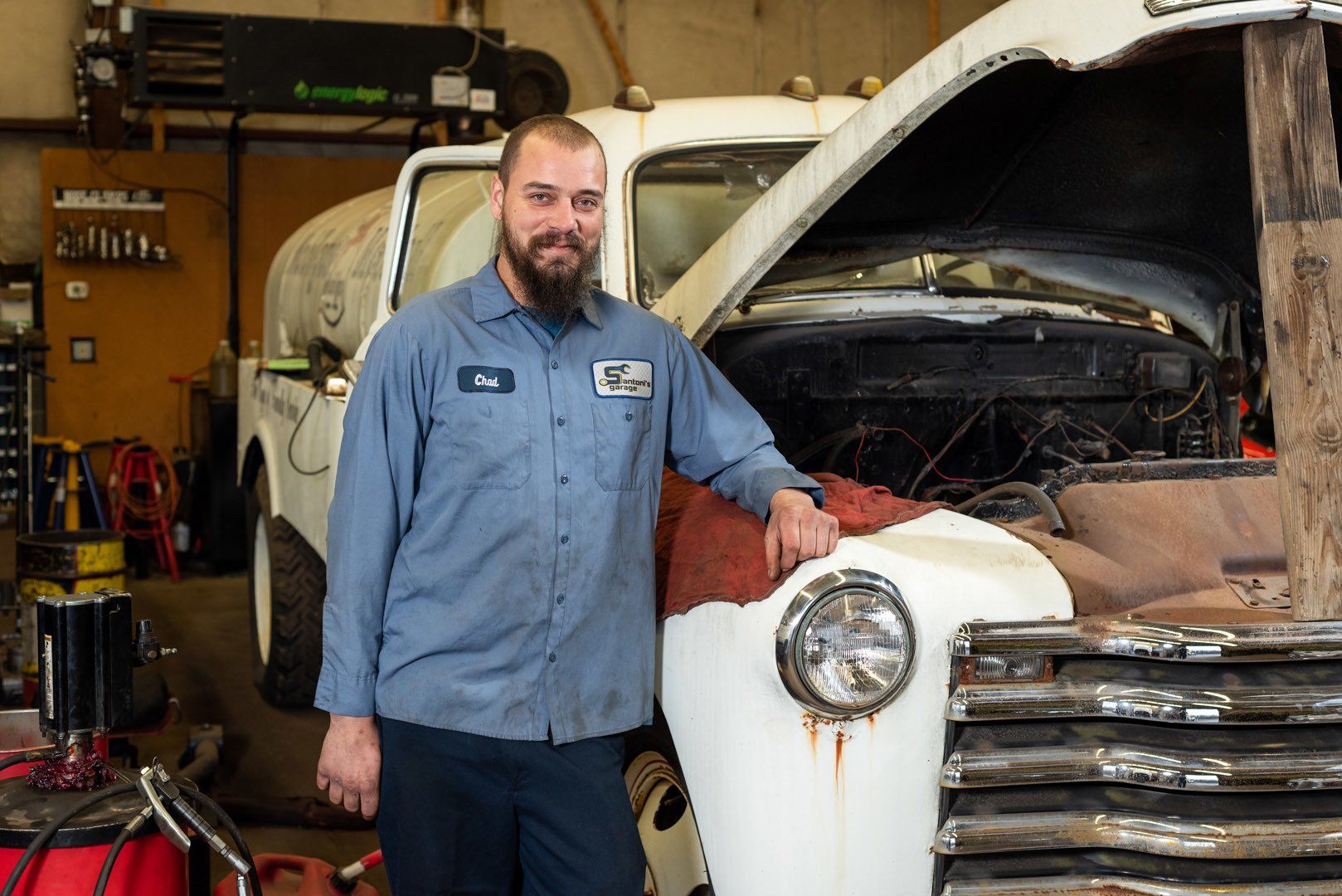 Mechanic standing by an old truck with open hood; in a garage.