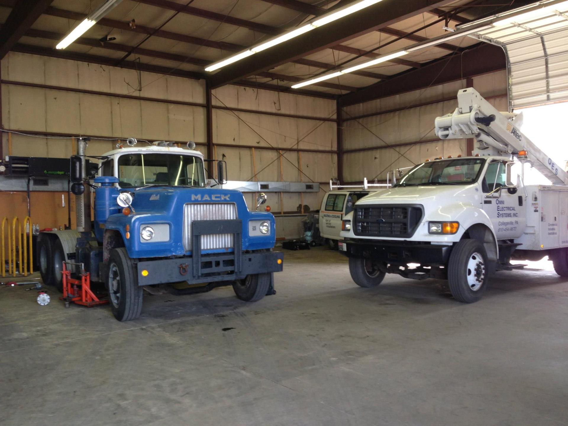 Blue Mack truck and white utility truck inside a garage.