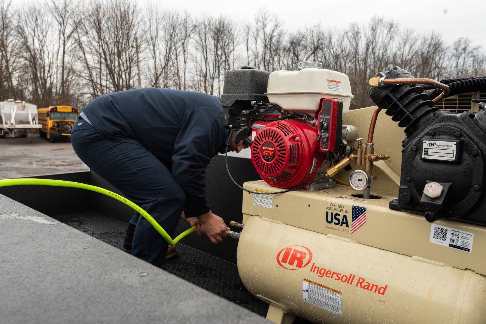 Man connecting a hose to a red engine compressor, outdoors.