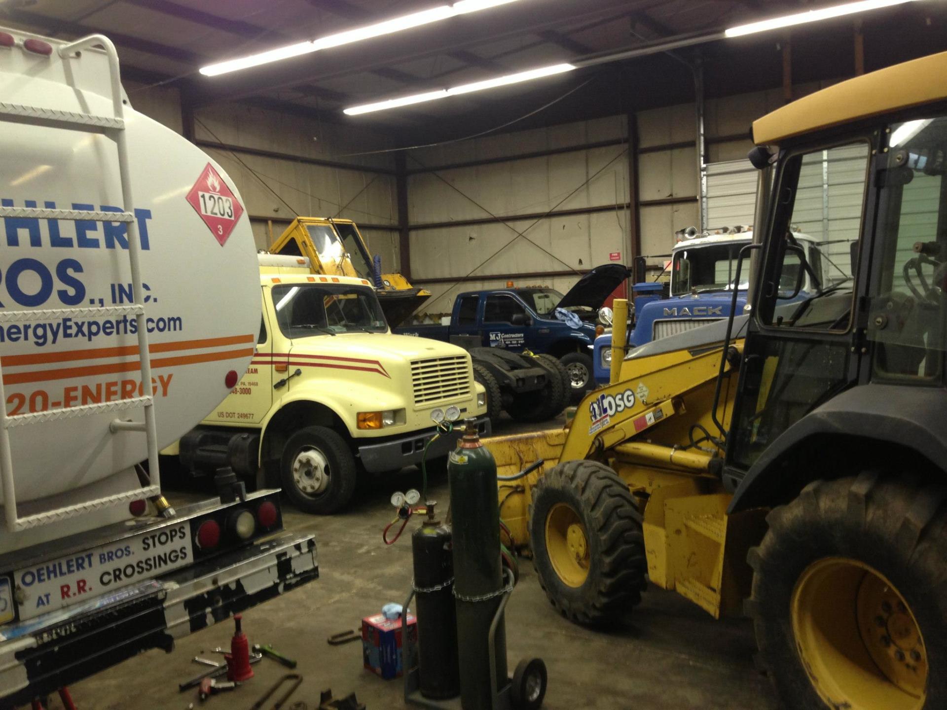 Yellow and white trucks, a backhoe, and welding tanks in a garage setting.